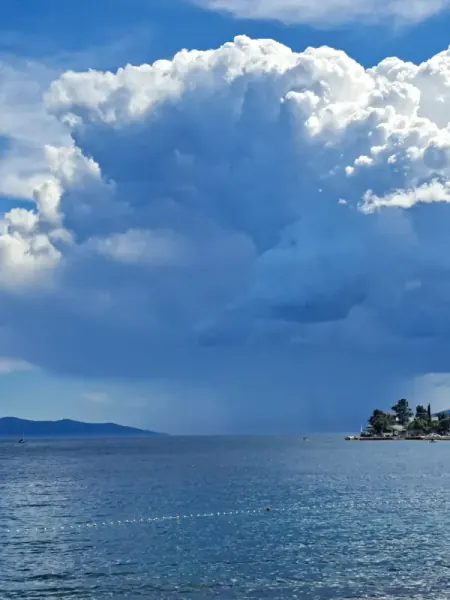 A Nevera storm cloud: a tall white cloud tower with a dark base and rain falling over the sea